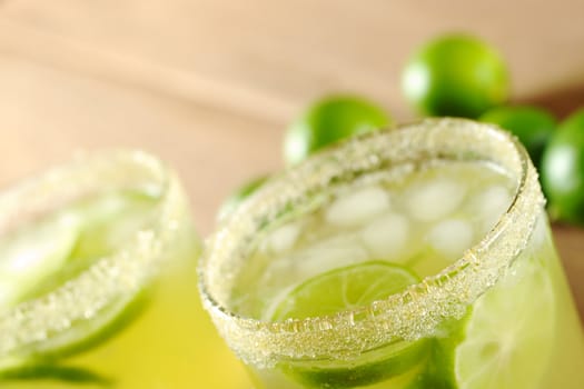 Fresh lemonade of green limes in sugar-rimmed glasses on wooden board with limes in the background (Selective Focus, Focus on the front rim of the first glass)