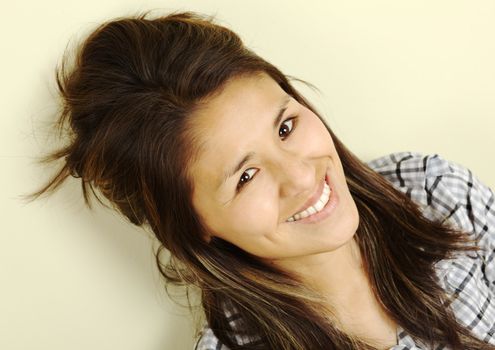 Beautiful young Peruvian woman with long brown hair smiling and leaning against a wall looking up into the camera (Selective Focus, Focus on the eyes)