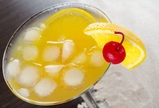 Maraschino cherry and orange slice on the rim of a cocktail glass with ice cubes, orange juice and orange slice inside photographed on white sand (Selective Focus, Focus on the rim of the glass, the cherry and the orange slice)