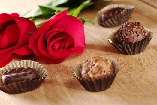 Red rose with truffles on wooden board (Selective Focus, Focus on the front of the rose and the dark chocolate truffle next to it)