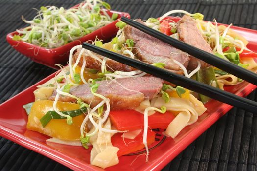 Duck breast with fried noodles, fresh vegetables and radish sprouts