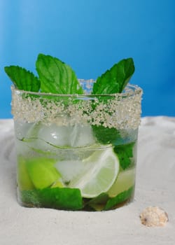 The Cocktail Mojito with Ice Cubes, Mint Leaves and Sugar Rim on Sand and with a seashell