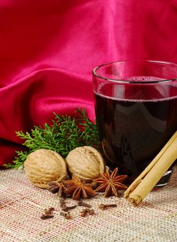 Hot spiced red wine with cinnamon, star anise, cloves, walnuts and a branch of evergreen with red background (Selective Focus)