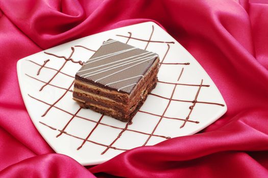 Tiramisu Cake served on a plate decorated with chocolate on red fabric