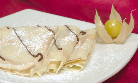 Palatschinken (Pancakes, Crepes) with chocolate and powdered sugar on a plate and a physalis fruit as decoration