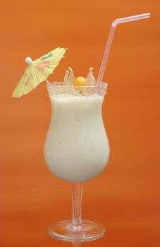 White Guanabana Smoothie in Cocktail Glass Decorated with a Paper Sunshade and a Physalis Fruit on Orange Background