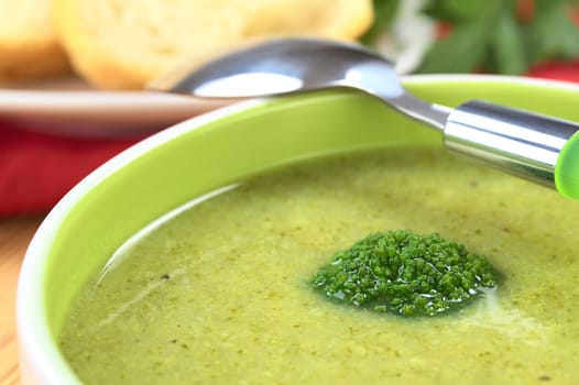 Cream of broccoli garnished with a broccoli floret on top with baguette slices in the back (Selective Focus, Focus on the broccoli floret on the soup)