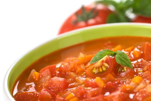 Chunky tomato soup made of tomatoes, carrots and onions and garnished with cherry tomato and a basil leaf (Selective Focus, Focus on the left cherry tomato and the right basil leaf)