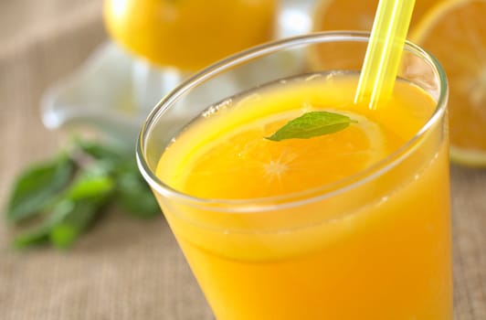 Freshly squeezed orange juice with drinking straws and orange slice, mint leaf on top of the juice (Selective Focus, Focus on the mint leaf in the glass)