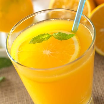 Freshly squeezed orange juice with orange slice and mint leaf on top of the juice with a blue drinking straw (Selective Focus, Focus on the mint leaf on top of the juice)