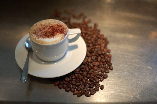 capuccino cup and some coffe beans steel  bar top