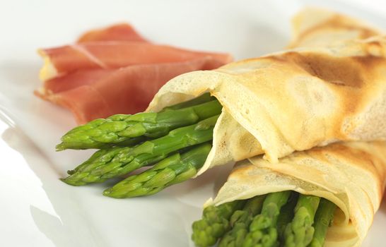 Green asparagus wrapped in crepes with ham in the background (Selective Focus, Focus on the horizontal asparagus heads)