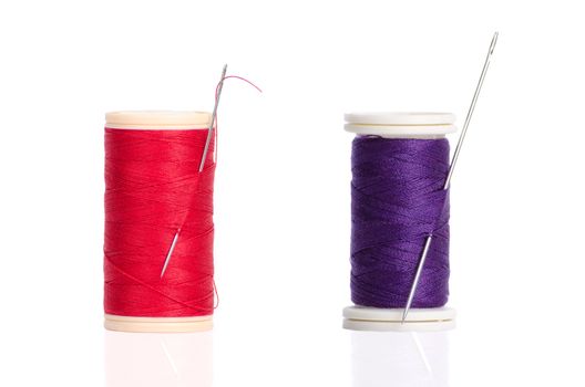 Two red and purple thread bobbin and needle isolated on white background.