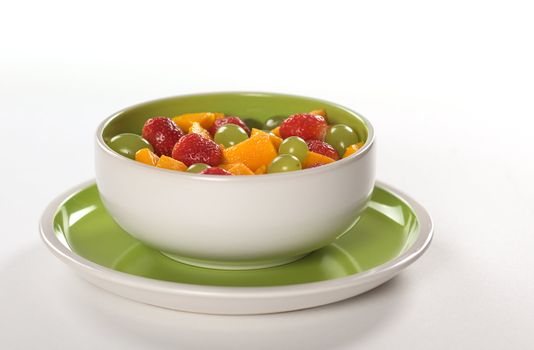 Healthy fresh fruit salad out of mango, strawberry and white grapes in green-white bowl photographed on white (Selective Focus, Focus on the middle) 