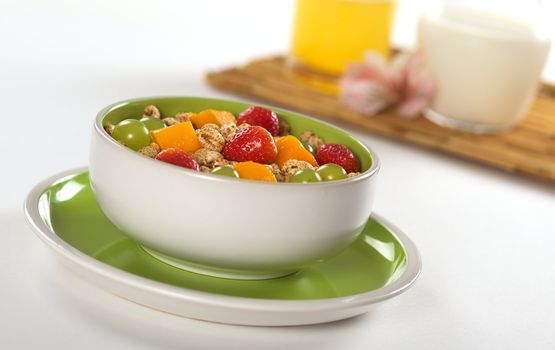 Fresh and healthy breakfast: Fruit salad out of mango, strawberry and white grape with puffed wheat cereal and orange juice and milk in the background (Selective Focus, Focus on the middle of the bowl) 