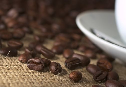 Coffee beans on fabric called Jute with a saucer and a coffee cup on the side (Very Shallow Depth of Field, Focus on the coffee bean on the left which is lit the most)