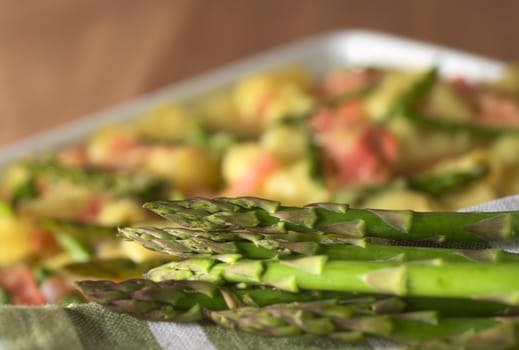 Fresh raw green asparagus with asparagus-ham-macaroni casserole in the back (Selective Focus, Focus on the head of the asparagus on top)