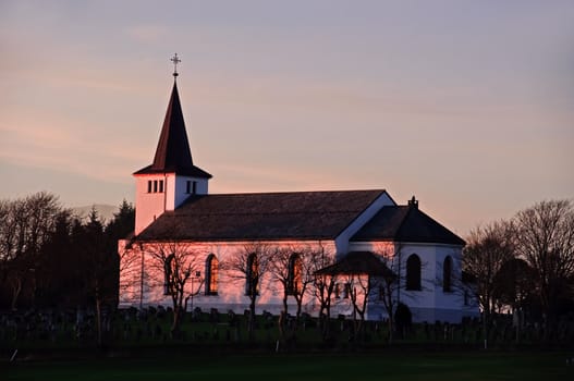 A white church is painted red in the sunset