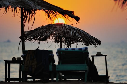 Exotic lean-to of palm leaves and deckchairs in evening