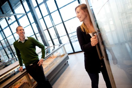 A couple smiling at eachother in a supermarket, shallow depth of field, focus on woman.