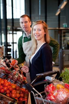 A woman buying fruit at a supermarket receiving help from a store clerk