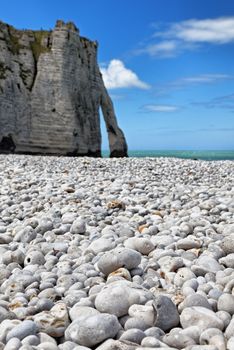 Image of the rocky beach and iconic natural arch from Etretat in Upper Normandy in North of France. Selective focus on the rocks in the first plane.