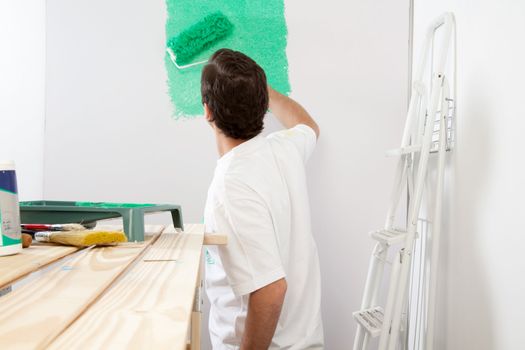 Man painting the wall with roller and brush, stepladder in background