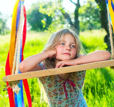 Young cute girl on swing with ribbons in the garden