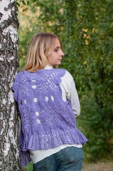 A girl in a lilac vest and white polo-neck sweater and jeans in a forest
