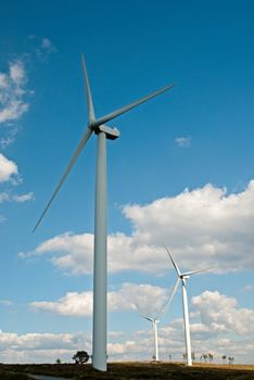 Wind turbines generating electricity with cloudy blue sky on the background.