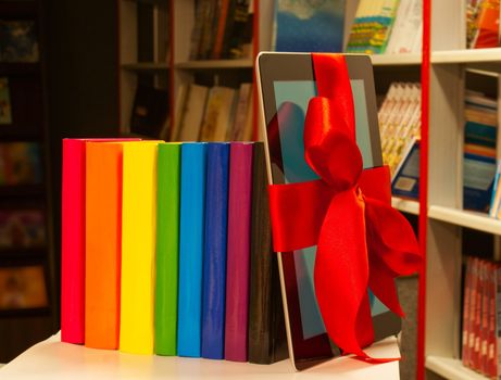 Electronic book reader tied up with red ribbon and row of books