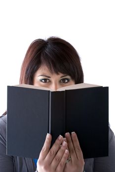 A young woman peeking over the top of a book she is holding up in front of her face.