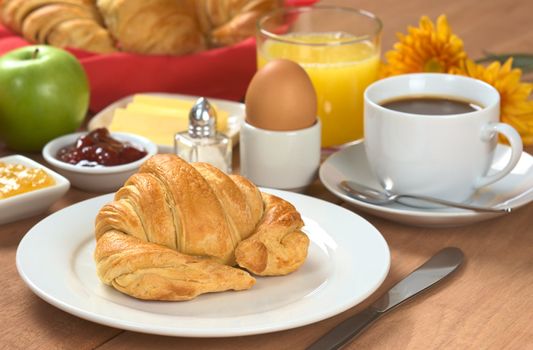 Delicious continental breakfast consisting of coffee, orange juice, croissant, boiled egg, jam, butter and apple (Selective Focus, Focus on the front of the croissant)