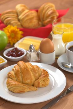 Delicious continental breakfast consisting of coffee, milk, orange juice, croissant, boiled egg, jam, butter and apple (Selective Focus, Focus on the front of the croissant)