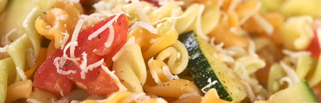 Colorful fusilli pasta with zucchini, tomato and grated cheese (Selective Focus, Focus on the outer side of the tomato)