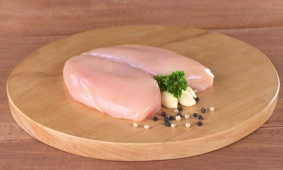 Raw chicken breast with white and black pepper corns, parsley leaf and garlic (Selective Focus, Focus on the front of the meat, the garlic and the parsley)