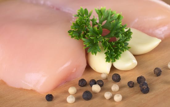 Raw chicken breast with white and black pepper corns, parsley leaf and garlic (Selective Focus, Focus on the front of the meat and the parsley)
