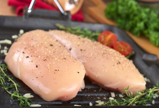 Raw chicken breast in frying pan seasoned with pepper, garlic and thyme (Selective Focus, Focus on the front of the left breast)