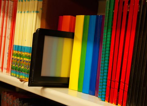 Row of colorful books and electronic book reader on the shelf