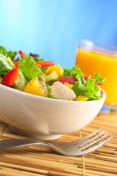 Fresh and healthy chicken salad with lettuce, mango, red bell pepper and cucumber with fresh juice in the back in front of blue background (Selective Focus, Focus on the front of the salad)