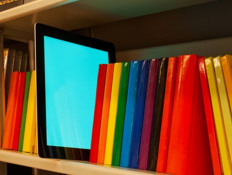 Row of colorful books and electronic book reader on the shelf