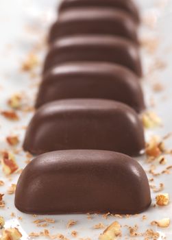 Chocolate candies filled with pecan nut arranged in a line on a long white plate  (Very Shallow Depth of Field, Focus on the front of the first candy)