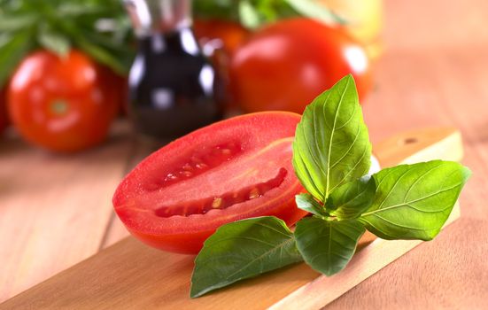 Fresh basil leaves with tomato halves with tomato and balsamic vinegar in the back (Selective Focus, Focus on the leaves on top and the right)