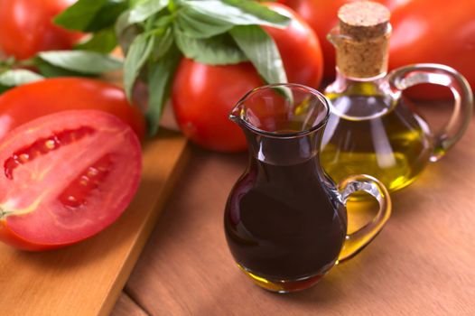 Balsamic vinegar with olive oil, tomato and basil in the background (Selective Focus, Focus on the front of the rim of the vinegar bottle) 