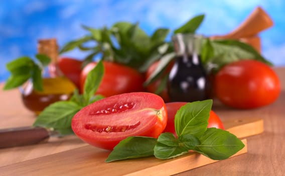 Fresh basil leaves with tomato halves with mortar, tomato, basil leaves, balsamic vinegar and olive oil in the back (Selective Focus, Focus on the basil in front)