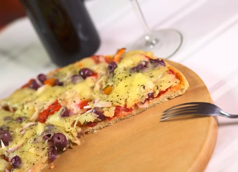 A partly eaten pizza on wooden plate on a table with wine in a restaurant (Selective Focus, Focus on the front of the pizza)