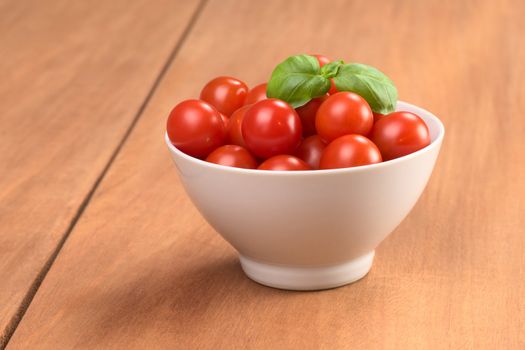 Cherry tomatoes garnished with basil leaf in small white bowl on wood 