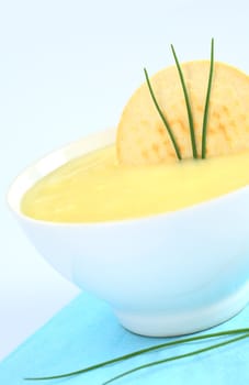 Fresh potato cream soup garnished with a cracker and chives on bluish background (Selective Focus, Focus on the cracker and the chives) 