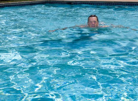 Baby boomer male floating in a backyard swimming pool on a hot summers day