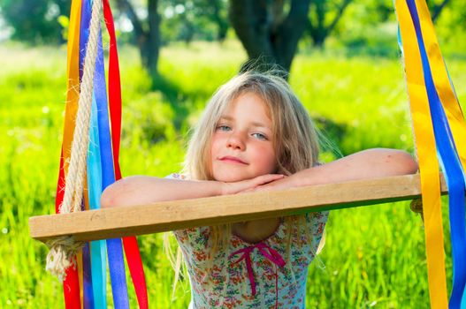 Young cute girl on swing with ribbons in the garden